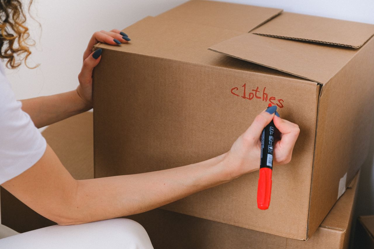 services-02 Vue rapprochée d’une femme étiquetant une boîte en carton avec un marqueur rouge à l’intérieur.