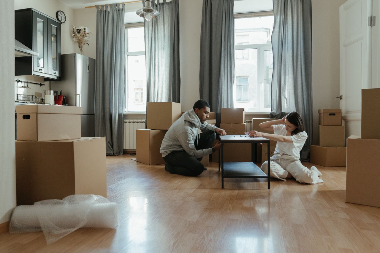 gallery-2 Young couple assembling furniture in their new apartment, surrounded by cardboard boxes.